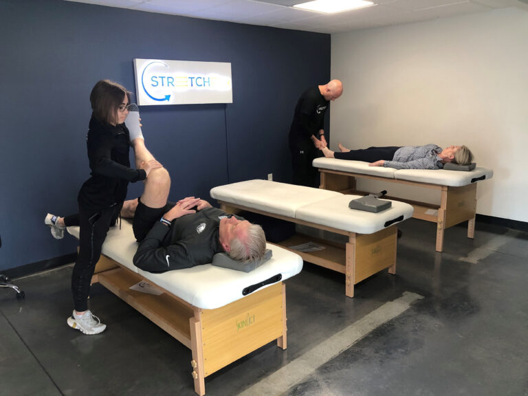 Two professionals stretching clients in a large room.