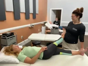 therapist assisting smiling woman with hip/leg stretch on table